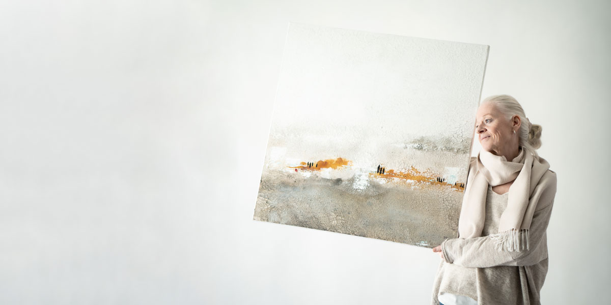 Künstlerin Sigrid Koller hält ihr Bild "Toskana" neben sich, während sie lächelnd in die Ferne blickt.